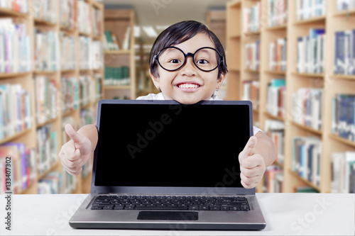 Child in library with laptop shows thumbs up