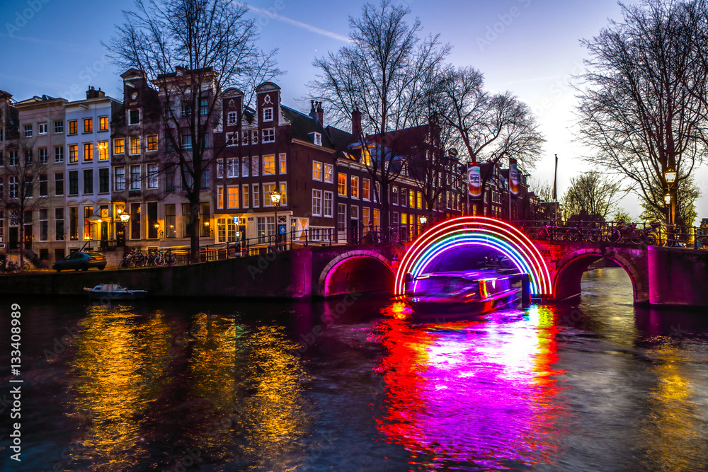 Fototapeta premium Amsterdam, Holandia - 10 stycznia 2017 r .: Statki wycieczkowe pędzą w nocnych kanałach. Instalacje świetlne na nocnych kanałach Amsterdamu w ramach Festiwalu Światła. 10 stycznia 2017 r. W Amsterdamie - Holandia.