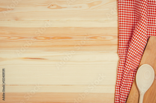 Top view of red checkered napkin or tablecloth on raw wooden table with visible planks, texture and copy space for text.