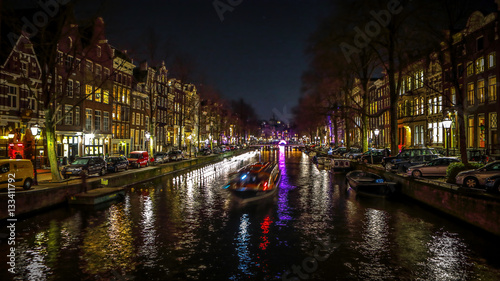 AMSTERDAM, NETHERLANDS - JANUARY 11, 2017: Beautiful night city canals of Amsterdam with moving passanger boat. January 11, 2017 in Amsterdam - Netherland.