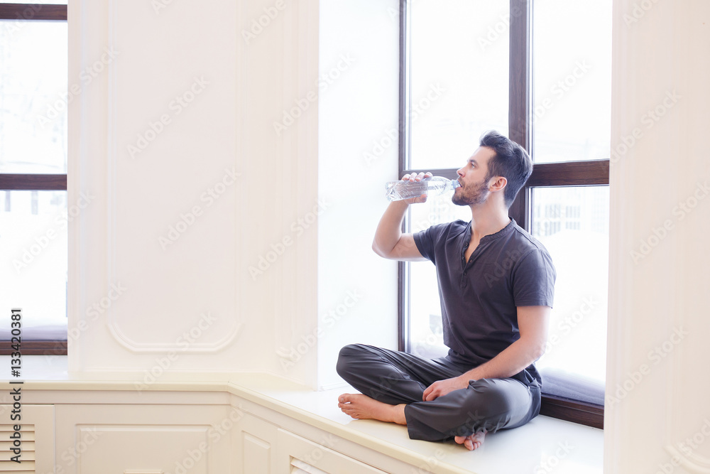 Beautiful woman drinking water while holding yoga mat in fitness studio