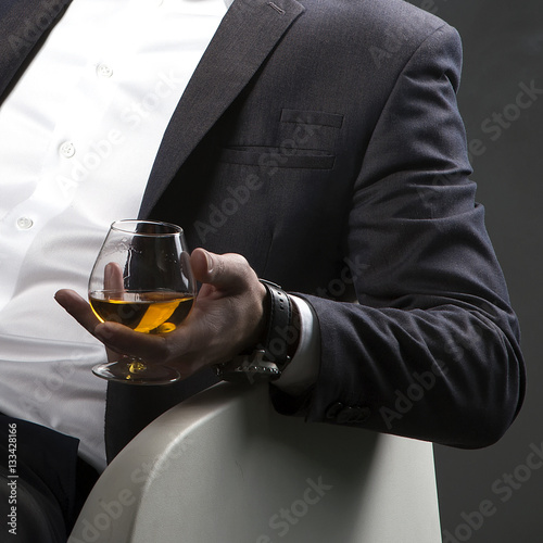 Cognac glass holding by man wearing suit and shirt over dark background