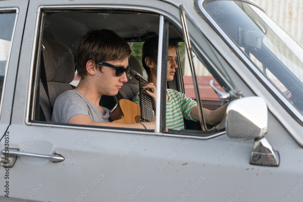 Naklejka premium Two young boys in the car. boy plays the guitar in the car. cheerful company of young people. journey together. fun pastime.