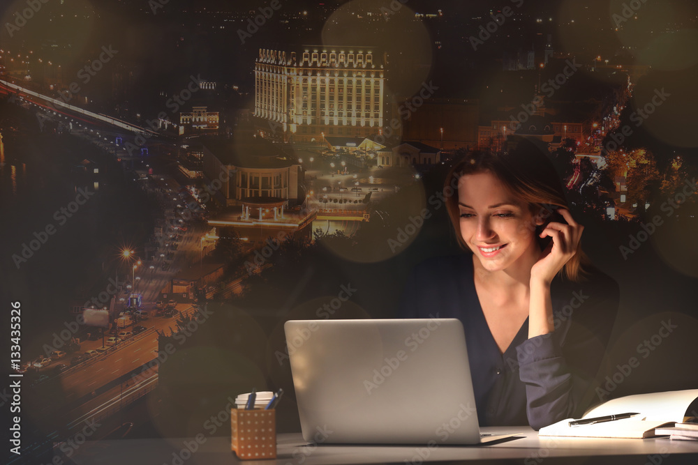 Young woman working with laptop and night cityscape on background