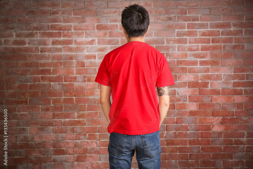 Young man in blank red t-shirt standing against brick wall Young man in blank red t-shirt standing against brick wall