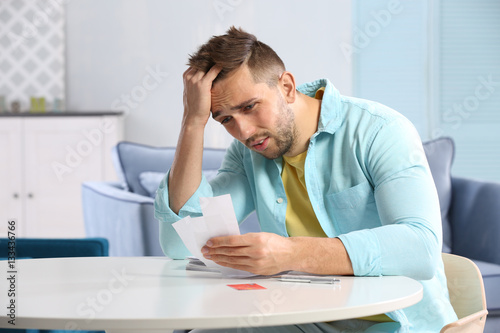 Confused young man calculating taxes at home