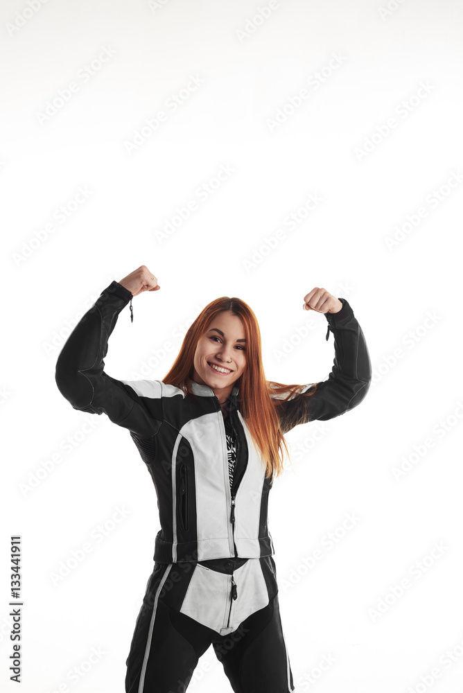 Happy and a lot of fun woman motorbiker. Femail in black and white protective dress with hands up on neutral background. Smiling girl with good mood. Win concept. Happy and a lot of fun woman motorbiker. Femail in black and white protective dress with hands up on neutral background. Smiling girl with good mood. Win concept.