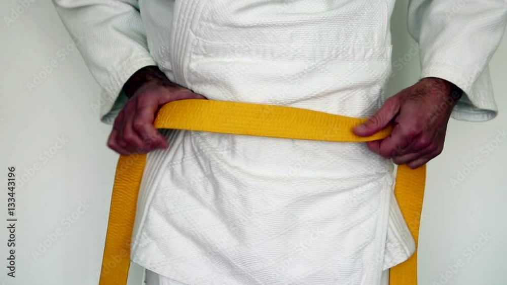 martial arts clothes, judo gi - a man tighten his yellow belt on a white kimono