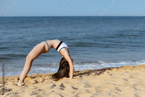 Back side view of acrobatic woman doing exercises on sandy beach sunny background outdoors