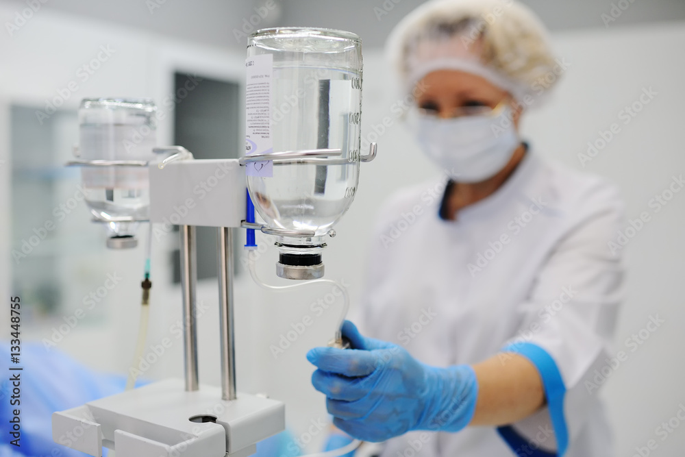 Doctor woman in medical mask and sterile gloves preparing a patient for surgery. Dropper into a vein close-up on a background of the surgical operational Doctor woman in medical mask and sterile gloves preparing a patient for surgery. Dropper into a vein close-up on a background of the surgical operational