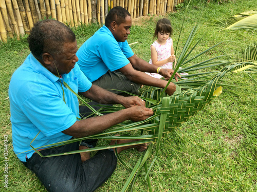 Fotografie Fijian men teach young tourist girl how to create a basket from