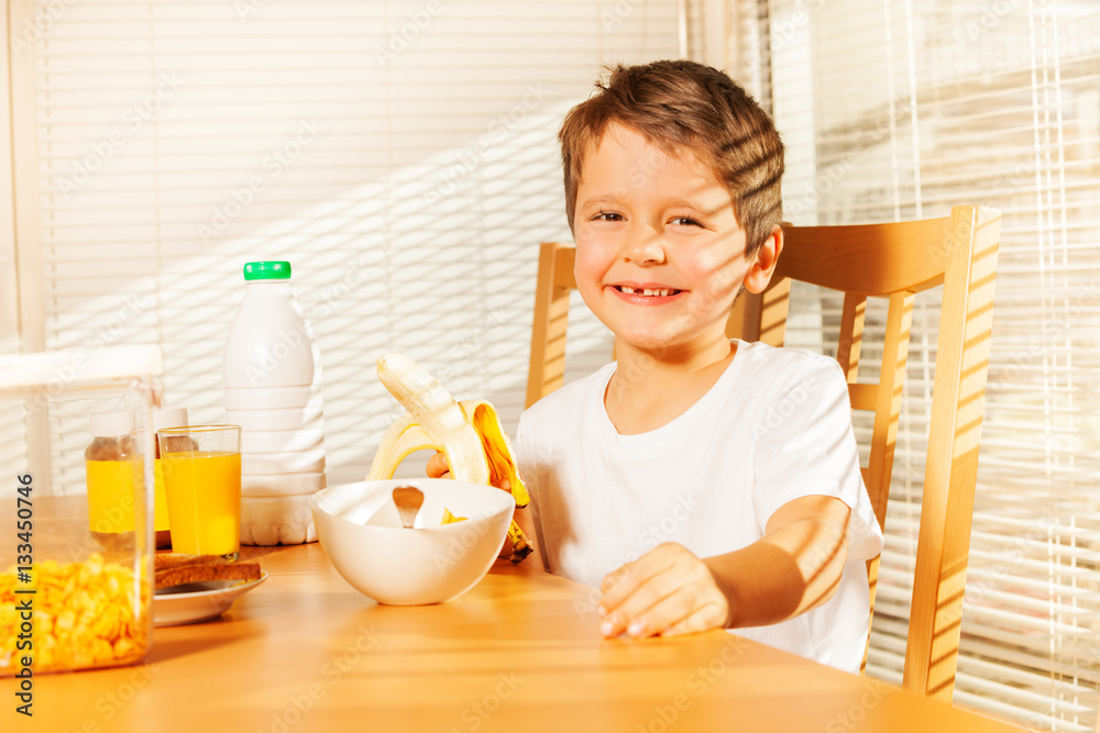 Smiling kid boy holding banana in the kitchen Smiling kid boy holding banana in the kitchen
