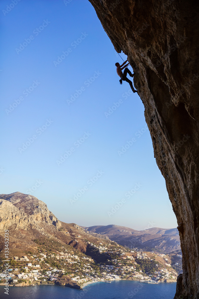 Young man climbing overhanging cliff against beautiful view of coast
