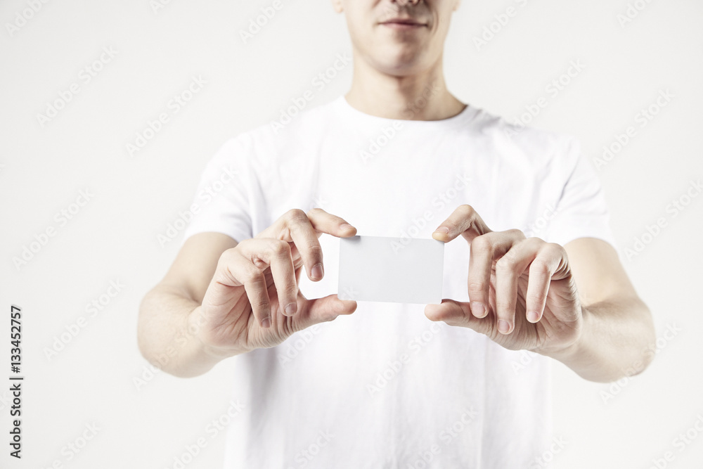 Close-up of man's hands holding a business card, guy wearing white t-shirt. White background in studio Close-up of man's hands holding a business card, guy wearing white t-shirt. White background in studio
