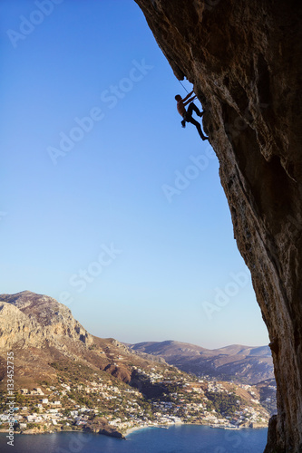Young man climbing overhanging cliff against beautiful view of coast