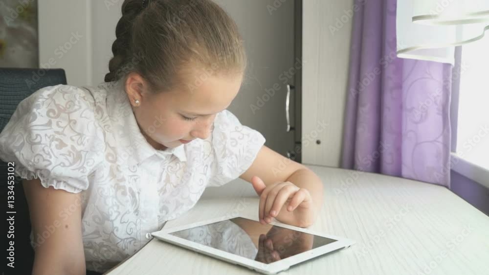 Teenager girl smiles while uses a digital tablet computer at the desk at home Teenager girl smiles while uses a digital tablet computer at the desk at home
