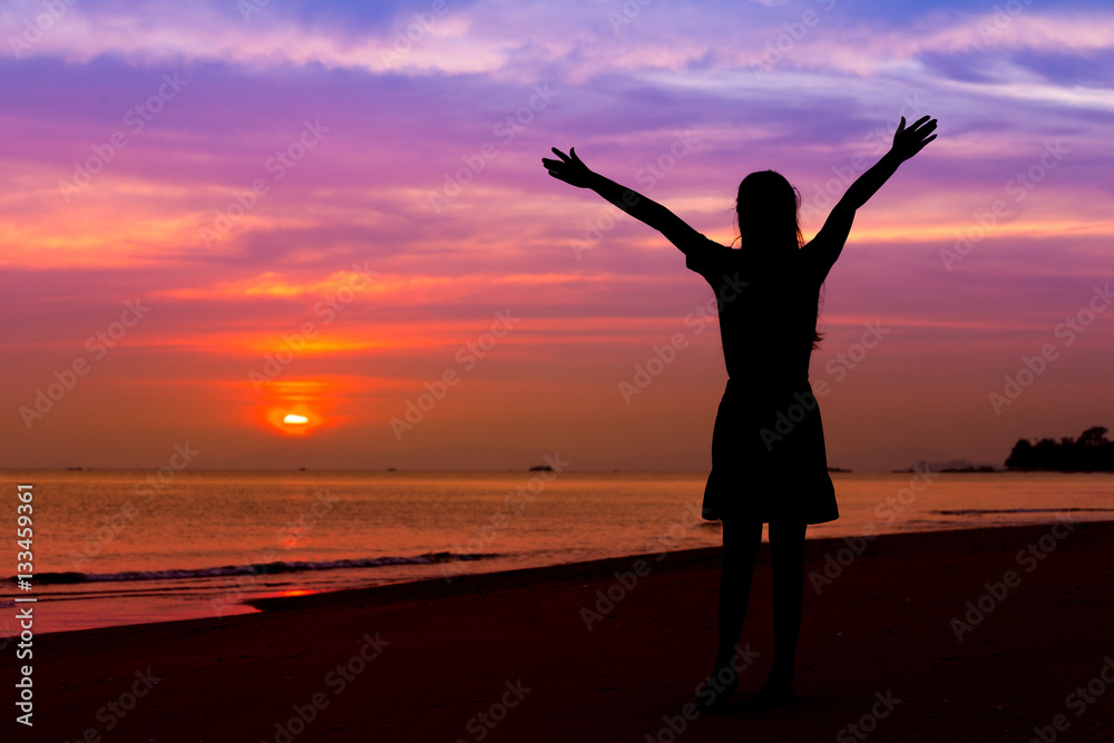 Silhouette of woman with hands up while standing on sea beach at