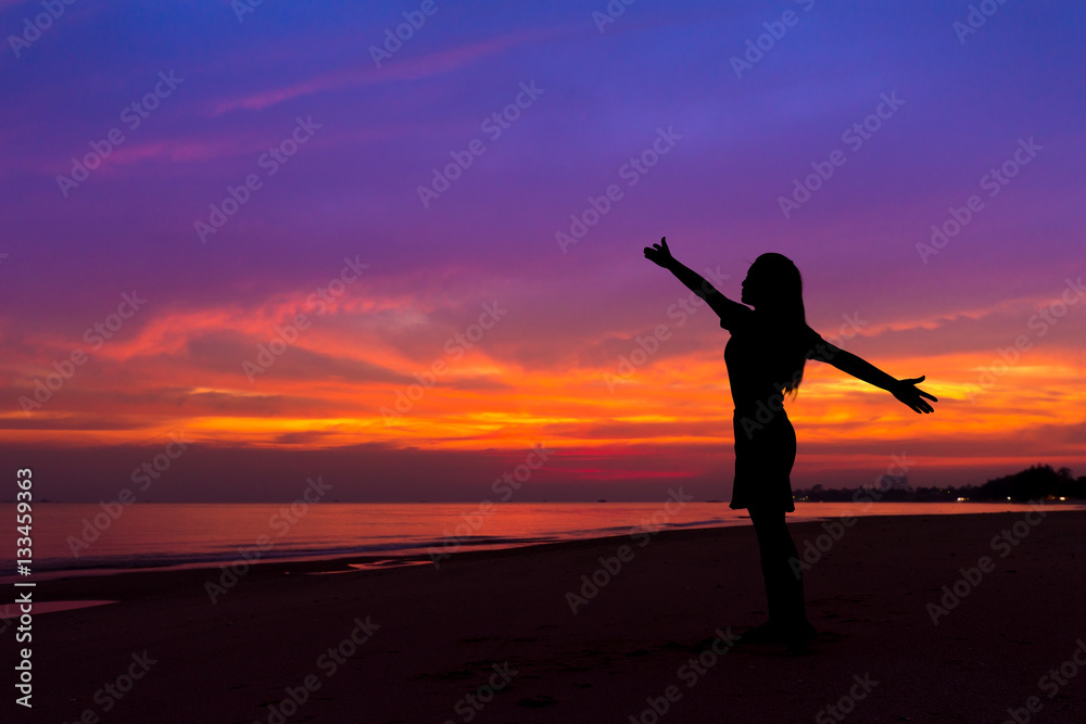 Silhouette of woman with hands up while standing on sea beach at
