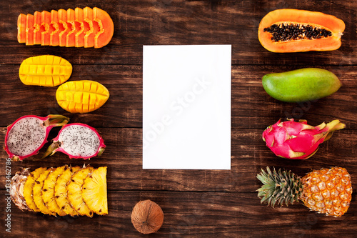 Tropical fruit on wooden background, with board in center, top view, copy space