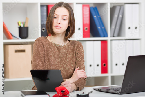 Woman looks through social networks in the office. Appraising looks into the tablet display. One eyebrow raised up, his lips pursed. photo