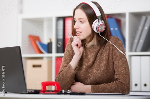 Beautiful female student with headphones listening to music and learning. Hold the handle in his hand and looking at laptop monitor