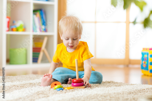 Portrait of cute child toddler boy assembling colorful pyramid toy on floor at living room