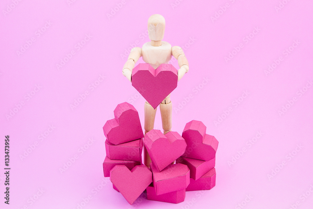Wooden dummy holding paper box red heart shape on pink backgroun