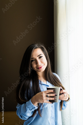 Young brunette girl in the morning with cup of coffee near window