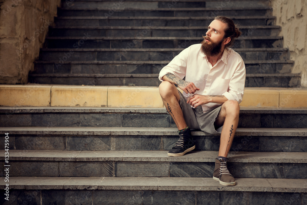 Beardead tattooed cool looking guy sitting in street on stairs