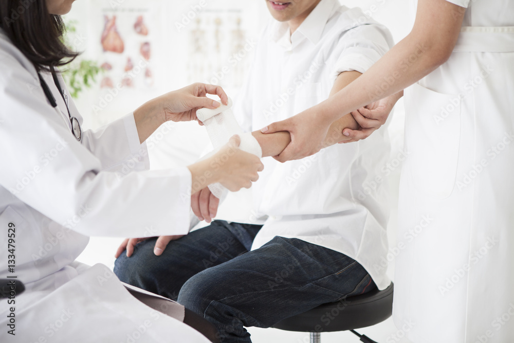 The doctor is wrapping a bandage in the hand of a man The doctor is wrapping a bandage in the hand of a man