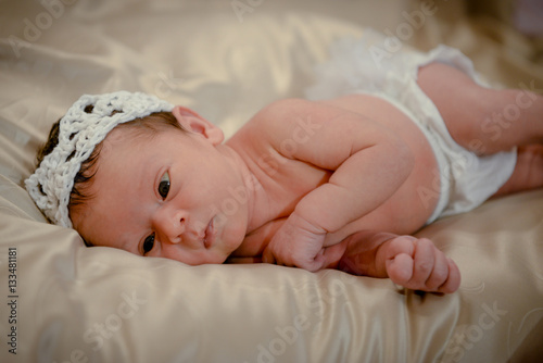 Portrait of a newborn baby infant toddler in bed. Close up top view portrait infant baby. Happy little newborn child girl lying in child bed.Happy smiling little girl.Healthy newborn girl after birth 