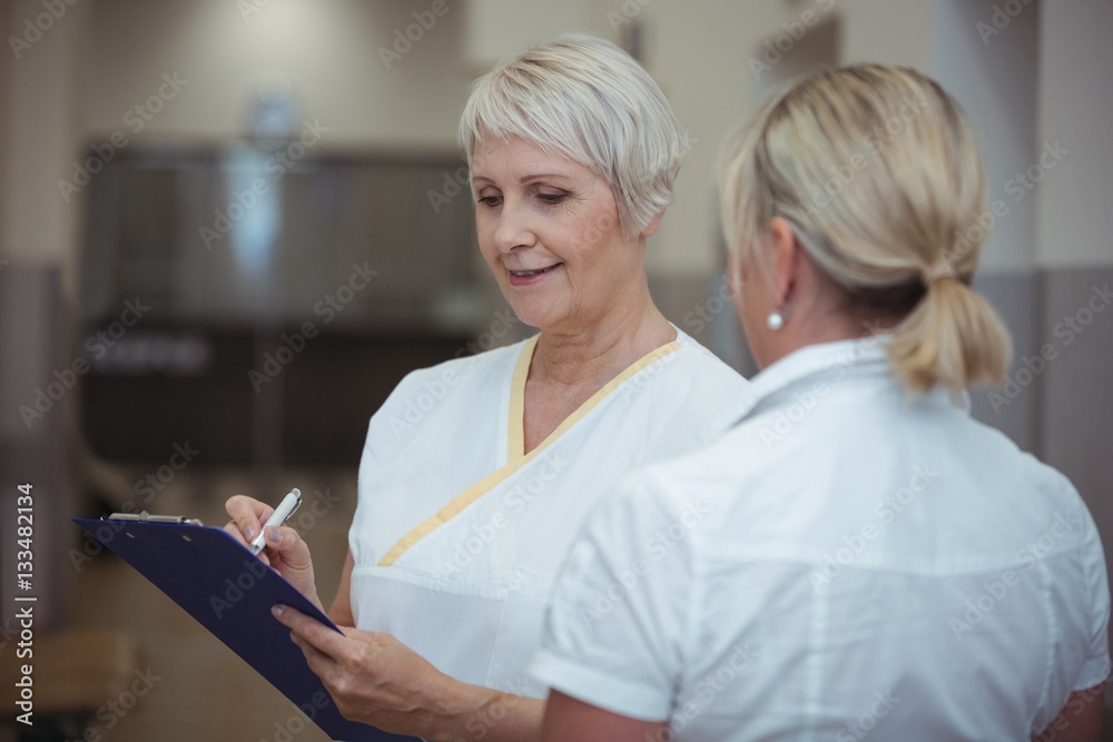 Two nurse having discussion over clipboard in corridor Two nurse having discussion over clipboard in corridor