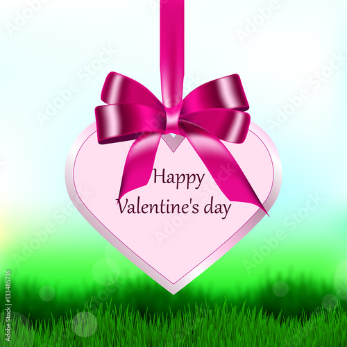 Heart on satin ribbon with a bow for the holiday Valentine's Day, which hangs over the green grass