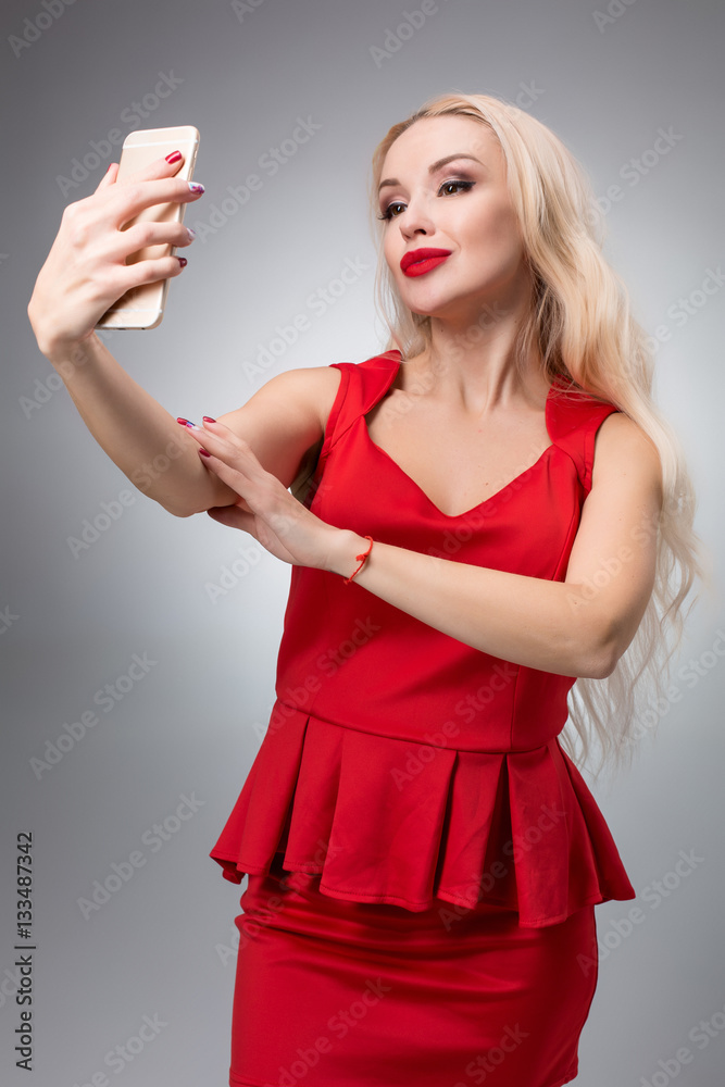 Naklejka premium Portrait of a Beautiful successful smiling girl doing selfie in red dress on light background