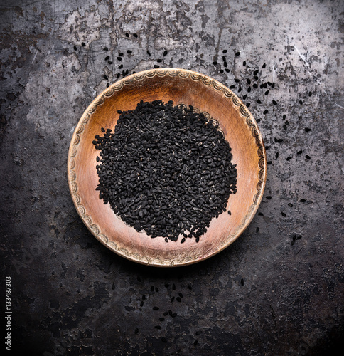 Black cumin seeds in rustic bowl on dark vintage background, top view. Nigella sativa seeds photo