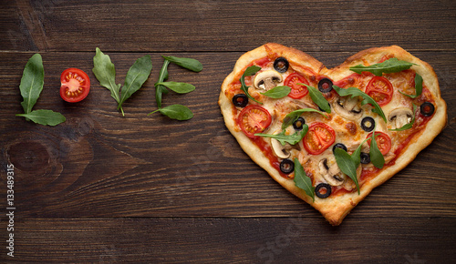 Valentines day pizza in heart shape with inscription love on dark rustic wooden background.