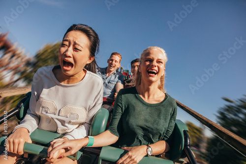 Friends cheering and riding roller coaster at amusement park photo