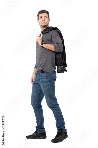 Side view of casual young man walking with jacket over shoulder looking behind. Full body length portrait isolated over white background.