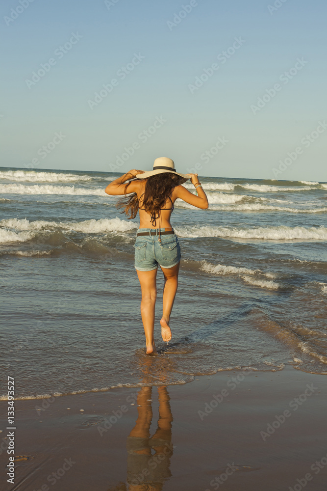 Young woman from behind, wearing summer hat and shorts jeans at