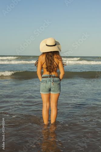 Young woman from behind, wearing summer hat and shorts jeans at