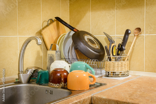 Dishes, cups, glasses, plates, forks, knives and spoons are drying close to the sink, after they have been washed in kitchen