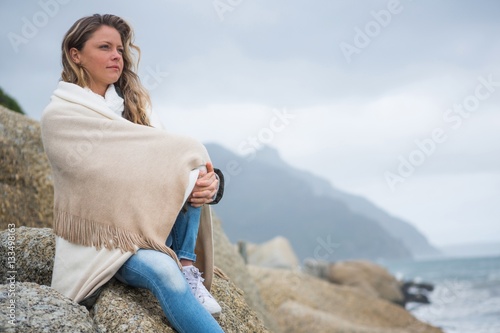 Fotografi Thoughtful woman wrapped in shawl sitting on rocks