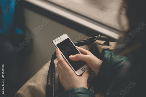 Close up view on the hands of a young woman holding a smart phone tapping the blank screen. Girl using device in a bus