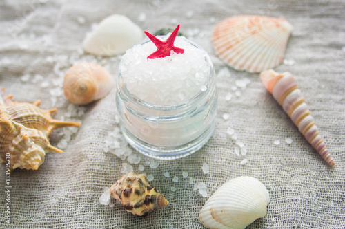 Seashells and a jar of sea salt on a grey cloth background. Spa concept.