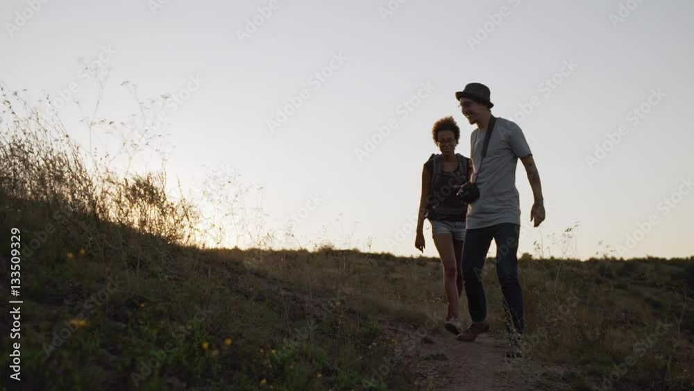 Caucasian male with camera glasses and hat alking outdoors with dark-skinned female with backpack in slowmotion Caucasian male with camera glasses and hat alking outdoors with dark-skinned female with backpack in slowmotion