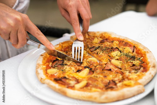 Woman cutting pizza with cheese, ham and pineapple. Hawaiian pizza.