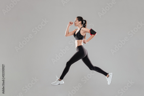 Pretty young fitness lady running over grey background