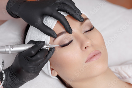 Cosmetologist making permanent makeup at beauty salon.