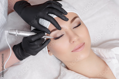 Professional cosmetologist wearing black gloves making permanent makeup