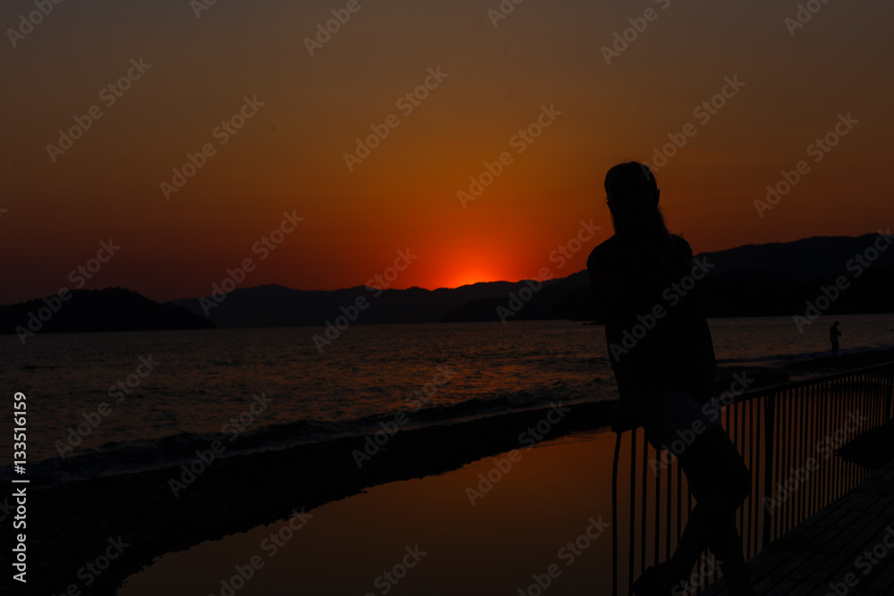 silhouette of a girl and basket flowers standing on the bank wide river in the rays the setting warm, beautiful sun